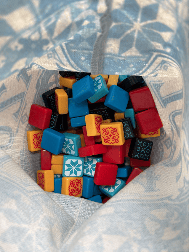 Inside a bag, containing the game tiles from Azul – lots of square tiles of differing colors