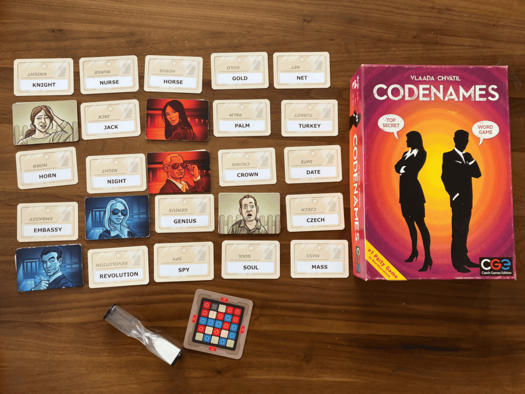 The game box for Codenames, it’s a yellow centre with circles out transitioning to purple, with a male and female presenting silhouette with speech bubbles saying “Top Secret” and “Word Game” with Codenames written in white across the top.