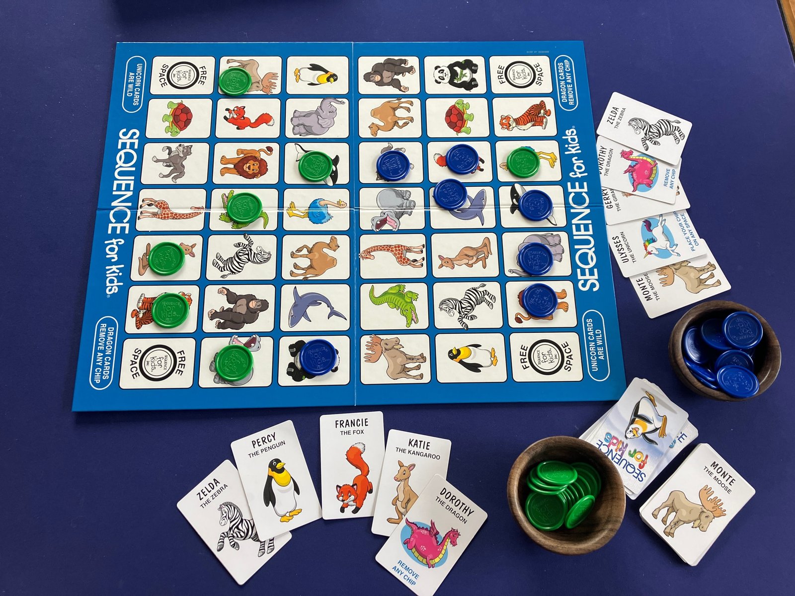 A game of sequence for kids, set up and in progress with the folding game board and blue and green playing chips