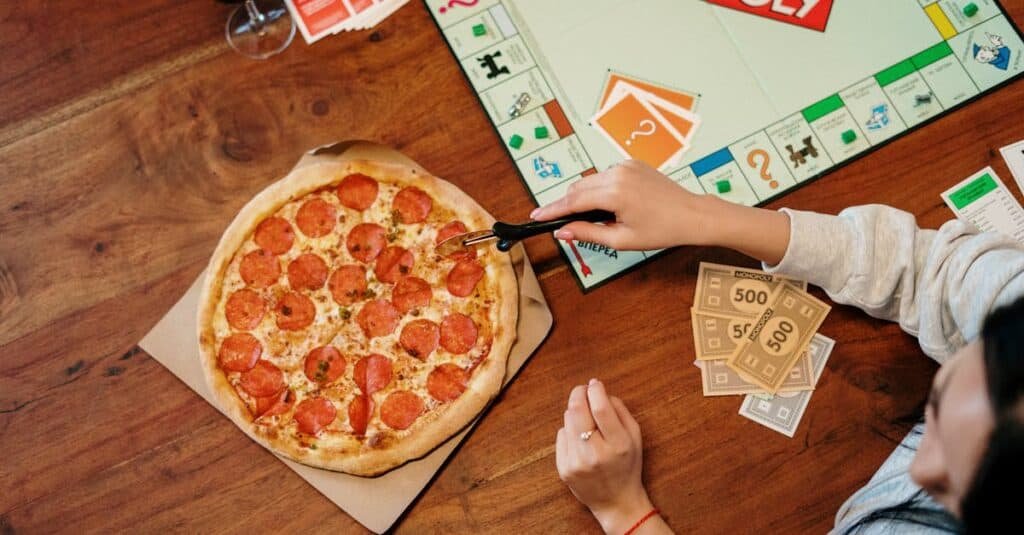 pexels-photo-4004418-4004418-1 Casual game night featuring Monopoly, pepperoni pizza, and red wine on a wooden table.