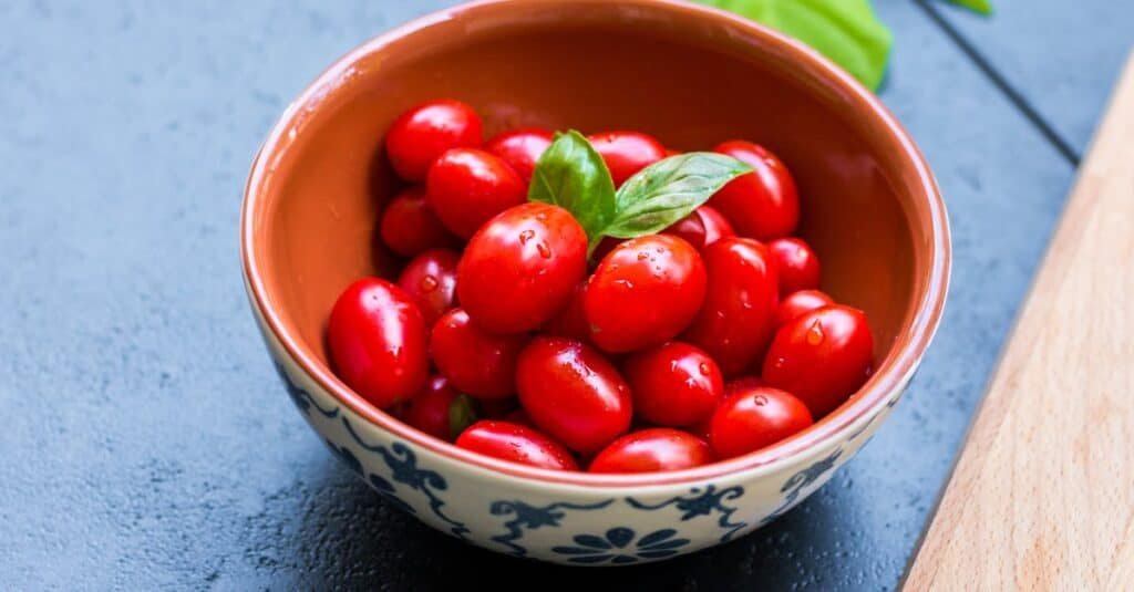 pexels-photo-533309-533309 Juicy cherry tomatoes in a bowl with basil leaves, showcasing fresh and healthy ingredients.